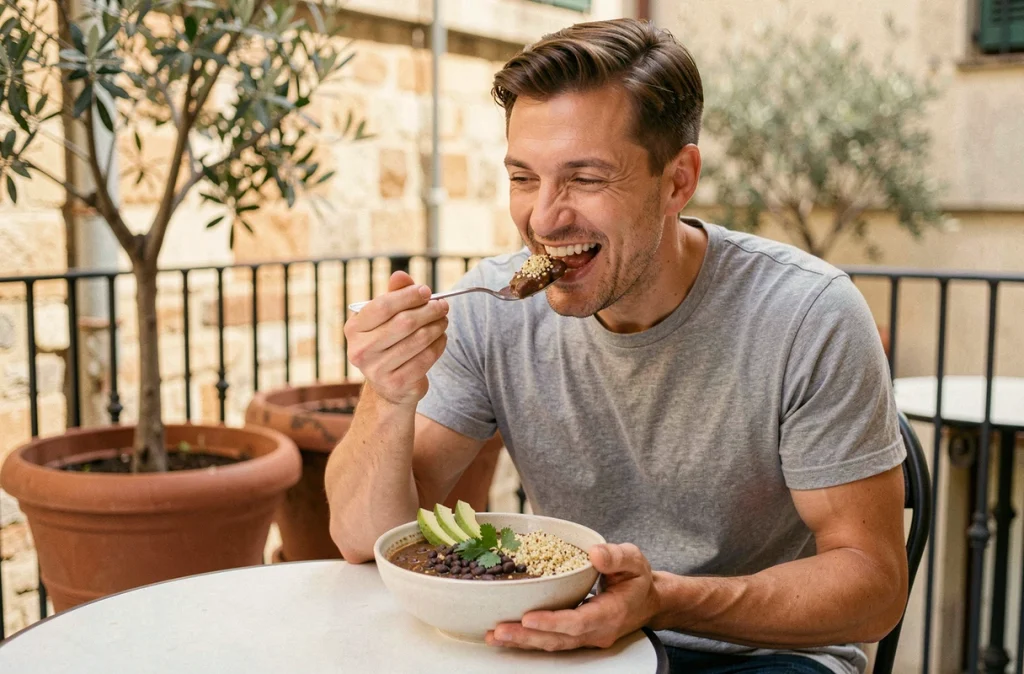 Homme souriant mangeant un bol de haricots noirs et quinoa sur une terrasse urbaine ensoleillée